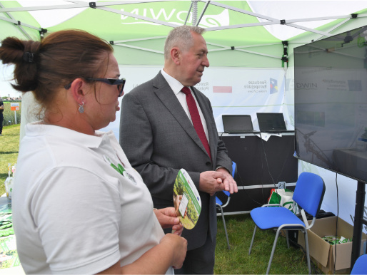 Minister Kowalczyk rozmawiał z doradcami WODR, którzy pracowali nad platformą eDWIN Minister rolnictwa Henryk Kowalczuk rozmawia z kobietą w średnim wieku, doradczynią WODR, na stoisku platformy eDWIN oraz spogląda na ekran telewizora na którym wyświetlone są dane dotyczące eDWIN.